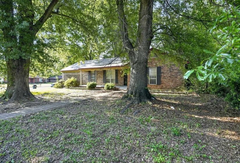 Brick-clad residence featuring mature trees, a covered porch entry, and a concrete walkway