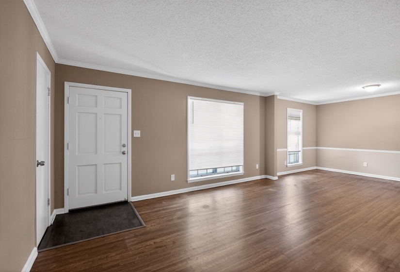 Spacious living area featuring wood-finish flooring, neutral paint tones, multiple windows with blinds, and white crown molding