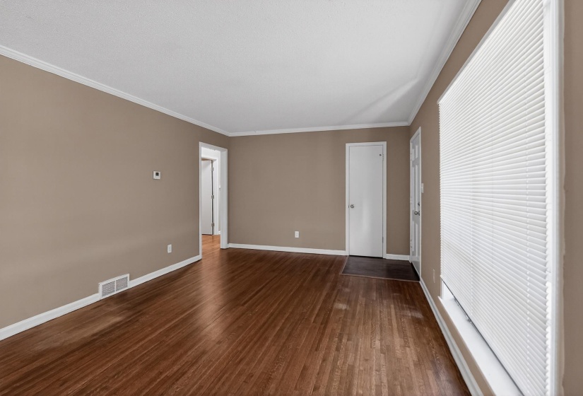 Spacious room featuring wood-finish flooring, neutral-toned walls, white crown molding, and a large window with horizontal blinds