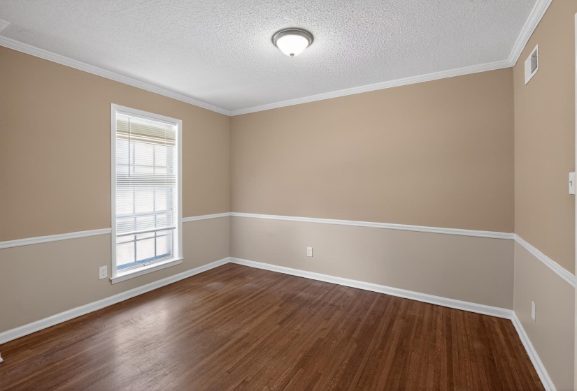 Room featuring wood-finish flooring, two-tone wall paint, white crown molding, and a window with horizontal blinds