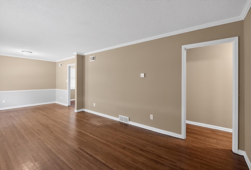 Hardwood flooring extends throughout this spacious room, featuring neutral-toned walls with a white chair rail and trim
