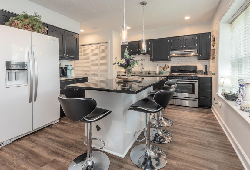Kitchen with white refrigerator with ice dispenser, gas range, a breakfast bar, and dark wood-style floors