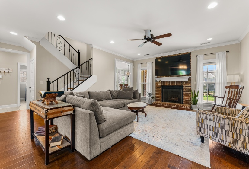 Spacious living area featuring rich wood-finish flooring, a brick fireplace, and ample natural light from multiple windows