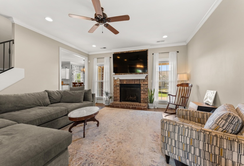 Living area featuring a brick fireplace with a wood mantle, wood-finish flooring, and crown molding