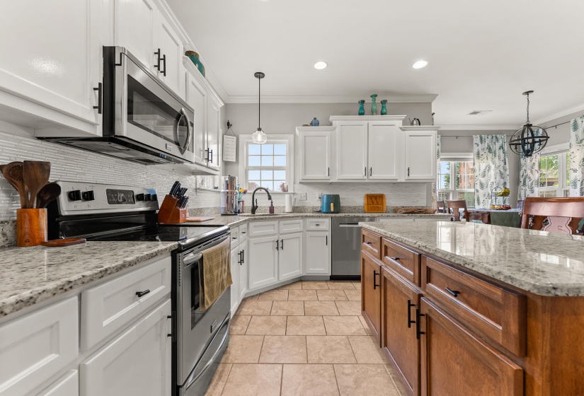 Kitchen featuring white cabinetry, a large kitchen island with wood-finish cabinetry, stainless steel appliances, speckled stone countertops, and tile flooring