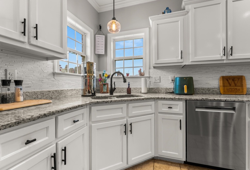 Bright kitchen featuring white shaker cabinetry, granite countertops, a tiled backsplash, and stainless steel appliances, including a built-in dishwasher