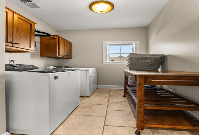 Laundry area featuring a window, tile flooring, wall-mounted cabinetry, and a ceiling-mounted light fixture