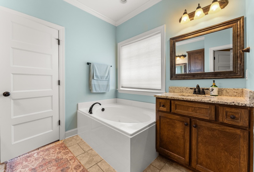 Bathroom featuring a white soaking tub with dark bronze fixtures, a vanity with a granite-style countertop, a wood-finish cabinet, and a framed mirror