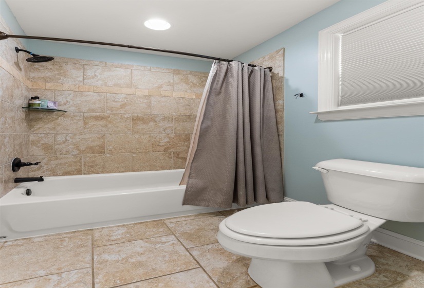 Bathroom with a tiled tub/shower combination, bronze-finish fixtures, and neutral-toned floor tile