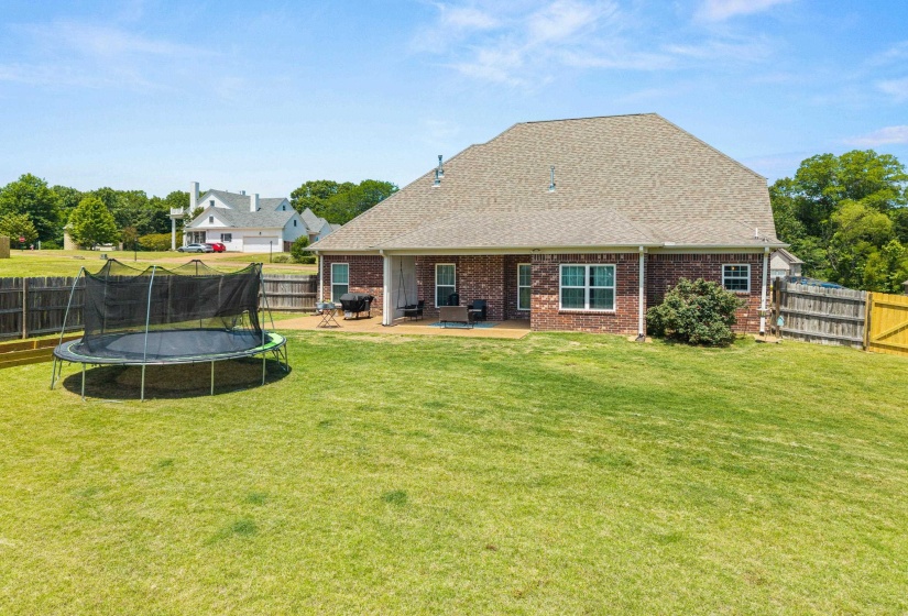 Expansive green lawn with a covered patio featuring a wood-finish deck and brick exterior