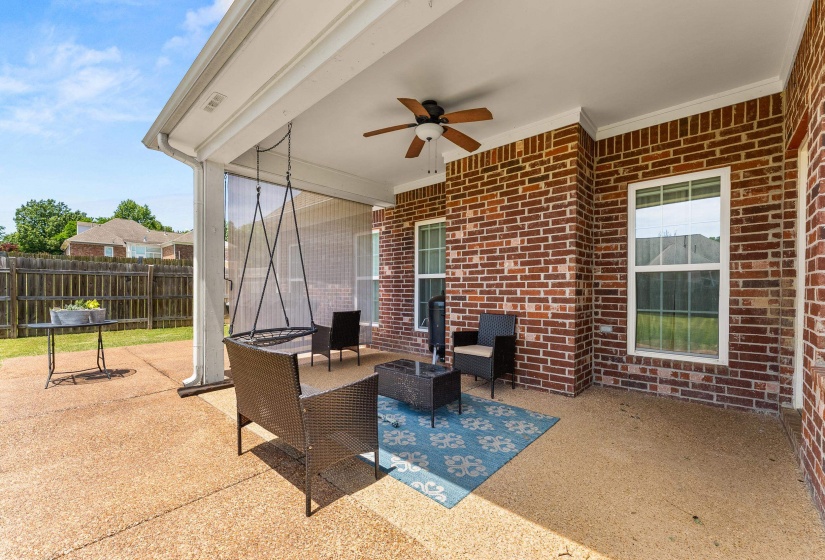 Covered patio featuring a ceiling fan, exposed aggregate concrete flooring, and a brick exterior