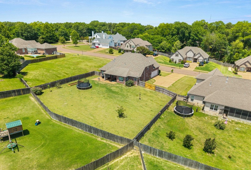 Fenced backyard featuring mature trees, a wooden fence, a small paved patio, and a well-maintained lawn