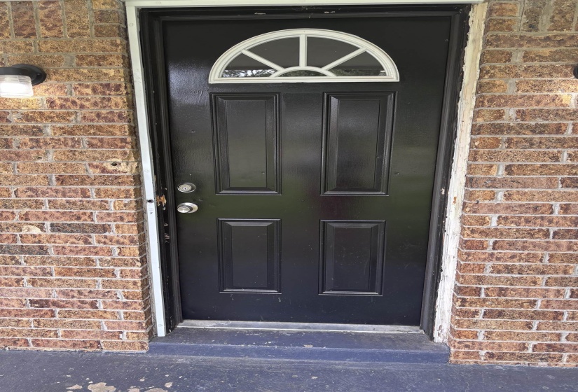 Black-paneled entry door with an arched transom window, flanked by two outdoor wall sconces and brick exterior siding