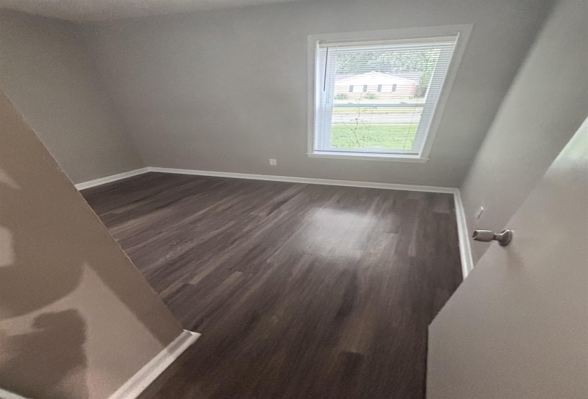 Room featuring wood-finish flooring, a double-hung window with white blinds, and white baseboards