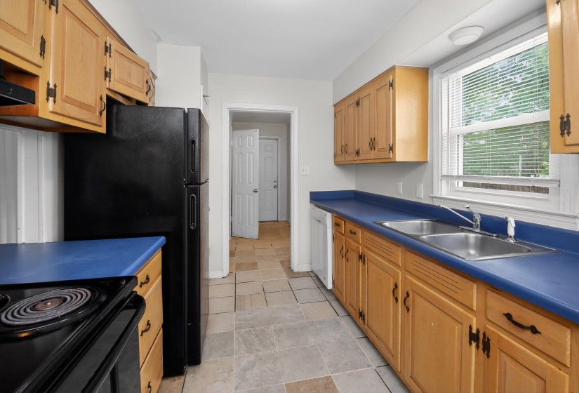 Kitchen featuring light wood cabinetry, blue countertops, a double basin stainless steel sink, a black electric range, and tile flooring
