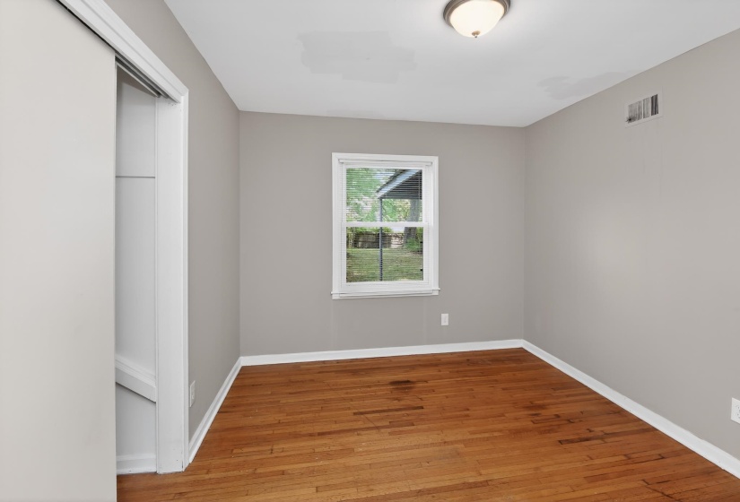 Hardwood flooring featuring a window with white trim, a flush-mount ceiling light fixture, and a sliding closet door