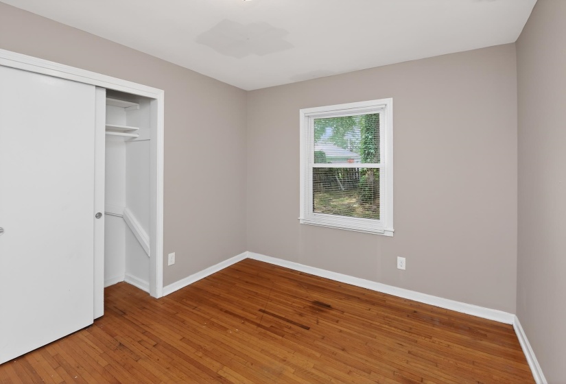 Bedroom featuring wood-finish flooring, a window with exterior visibility, and a closet with sliding doors and interior shelving