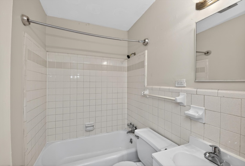 Bathroom featuring a white subway tile surround with a decorative band, a bathtub with a shower fixture, and a single vanity with an integrated sink