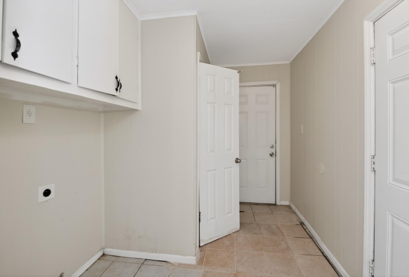Utility room featuring upper cabinetry with black hardware, neutral wall paneling, and ceramic tile flooring