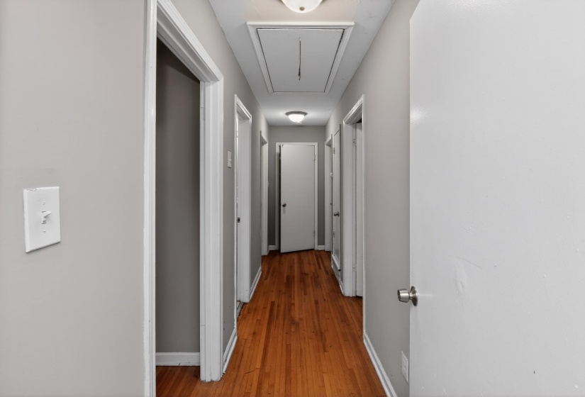 Hallway featuring wood-finish flooring, light gray wall paint, white trim, and multiple white interior doors