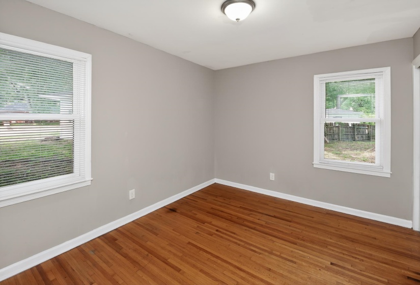 Room featuring wood-finish flooring, light gray walls, white baseboards, and two windows with white blinds