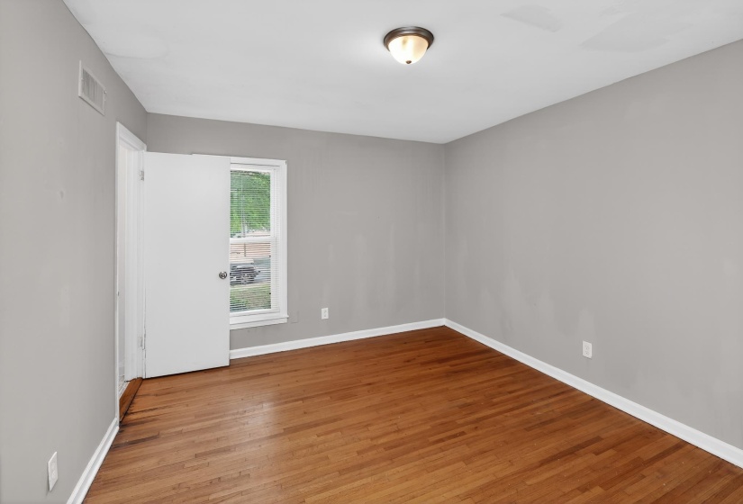 Room featuring wood-finish flooring, a single window, and a white interior door with a round knob