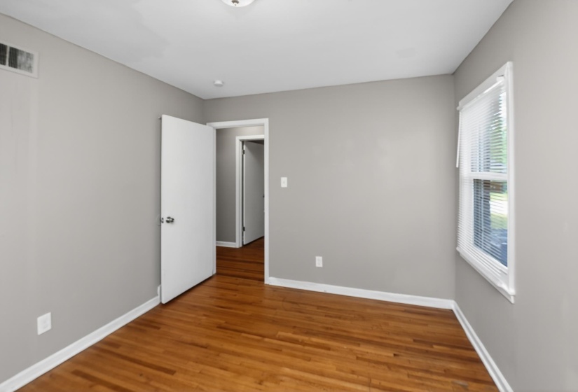 Room featuring hardwood flooring, light grey walls, white baseboards, and a window with blinds