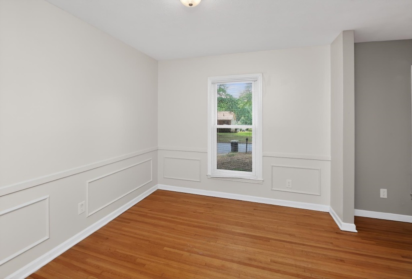 Hardwood flooring throughout, featuring a window with natural light, wainscoting detail, light-colored walls, and a ceiling-mounted light fixture