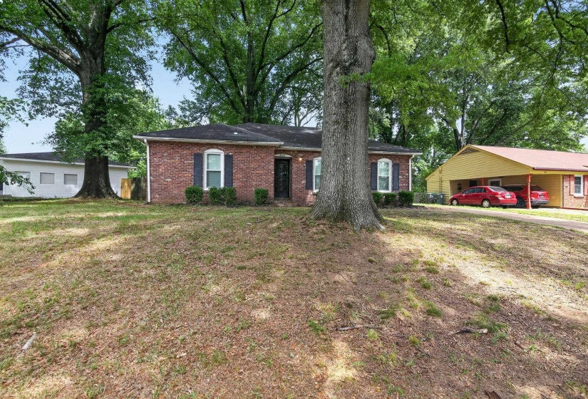 Brick exterior featuring a covered entry, dark shutters, and a sloped front yard