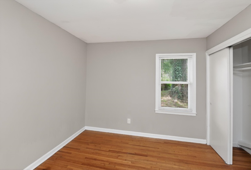Bedroom featuring light gray wall paint, wood-finish flooring, white baseboards, a single window with white trim, and a sliding closet door