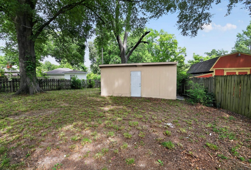 Expansive outdoor space featuring a detached storage shed with a white door, mature trees, and perimeter fencing