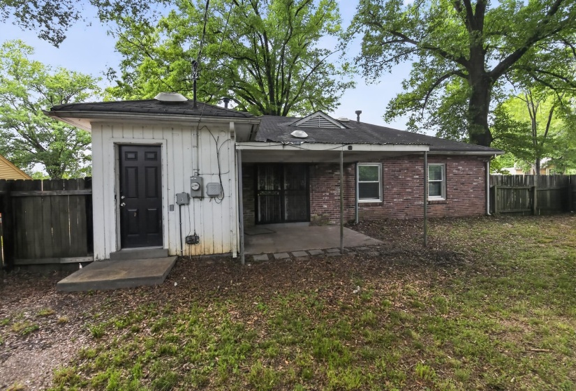 Rear exterior featuring a brick facade, white siding, covered patio area, and a fenced yard with mature trees