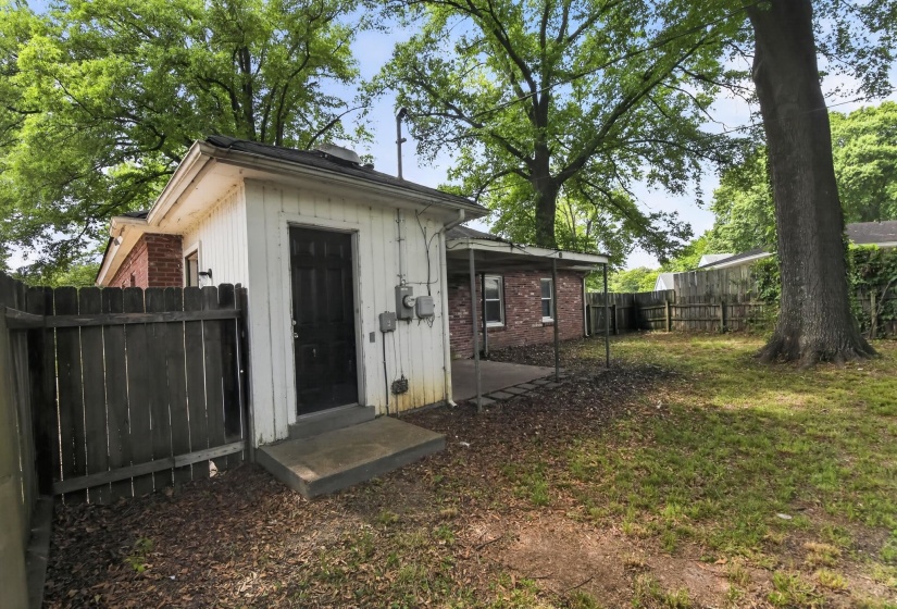 Detached utility building featuring a solid door, concrete stoop, and adjacent wood privacy fence