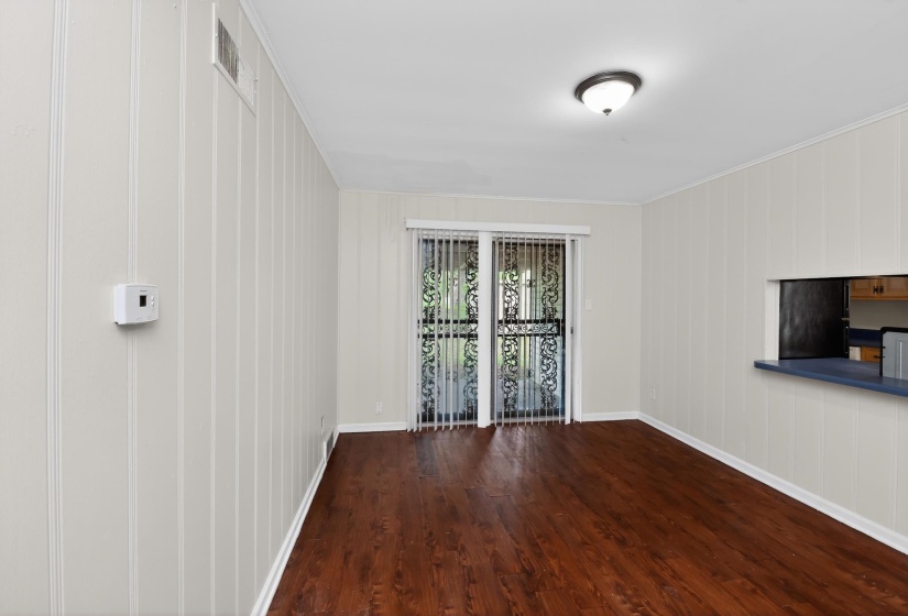 Spacious interior featuring wood-finish flooring, white vertical wall paneling, and a pass-through window with a blue countertop
