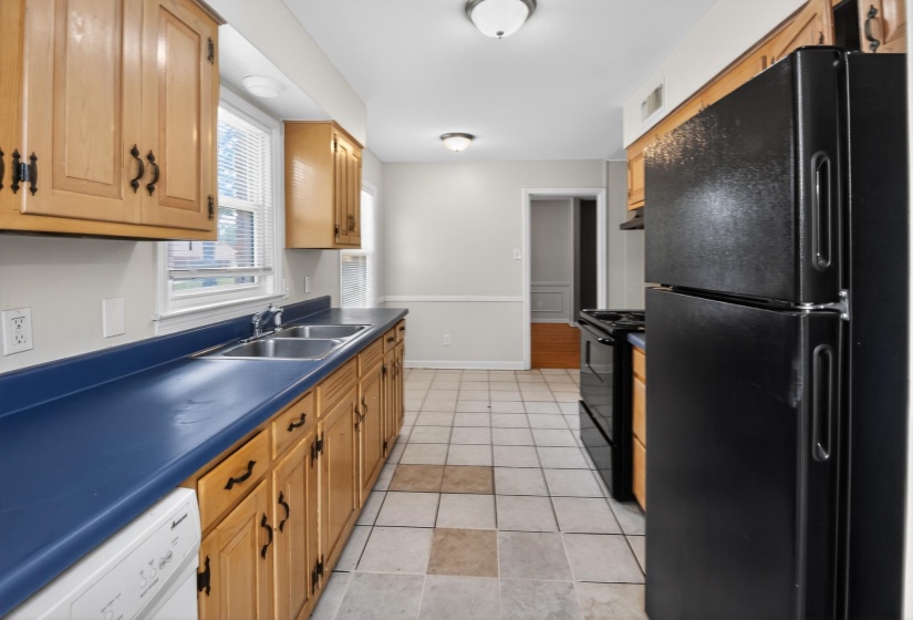 Kitchen featuring wood cabinetry, blue countertops, a double basin stainless steel sink, tile flooring, and black appliances