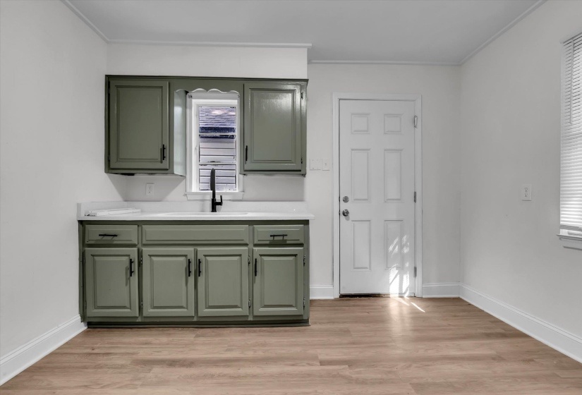 Kitchenette area featuring sage green cabinetry, white countertops, a black gooseneck faucet, and wood-finish flooring