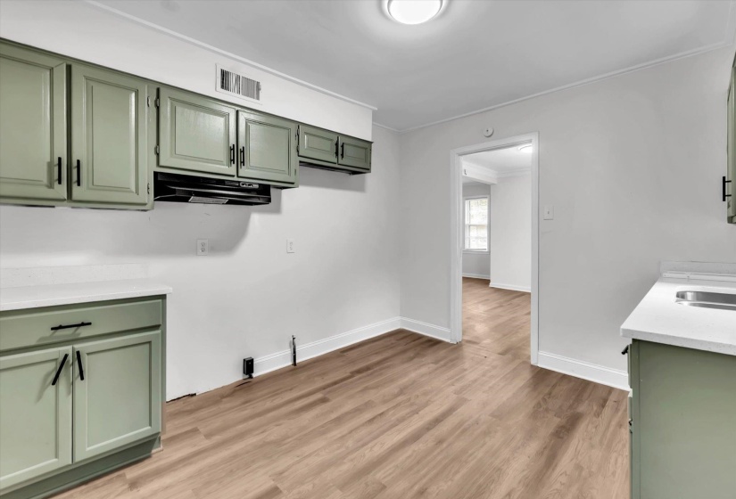 Kitchen area featuring sage green cabinetry with black hardware, white countertops, and wood-finish flooring