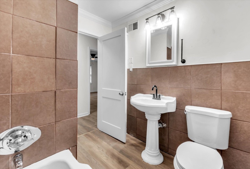 Bathroom featuring a pedestal sink, toilet, and a tiled accent wall