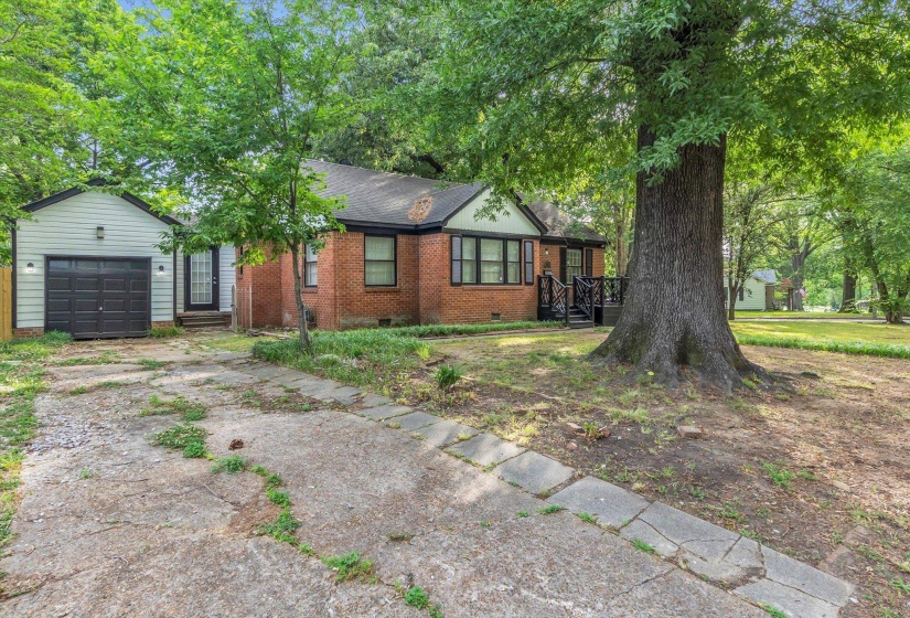 Brick exterior residence featuring a detached garage with horizontal siding, a covered porch with black railings, and a mature tree