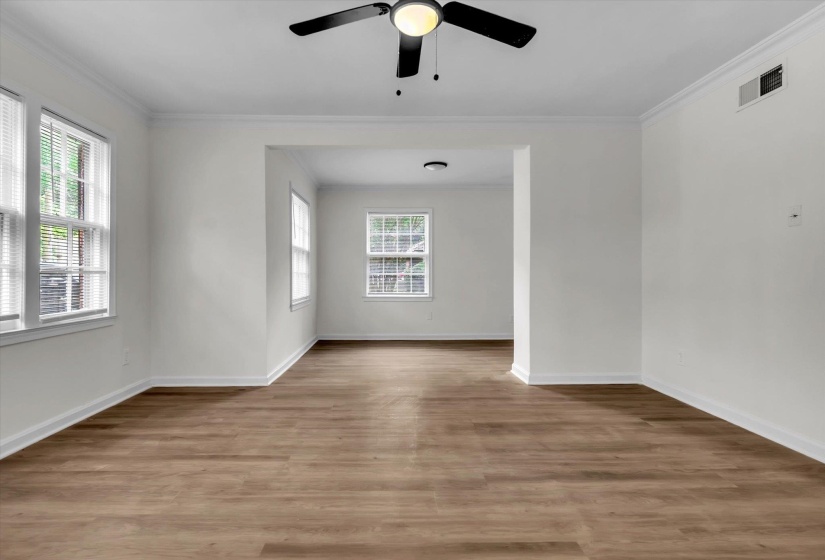 Spacious room featuring wood-finish flooring, white walls, multiple windows with blinds, crown molding, and a ceiling fan with integrated lighting