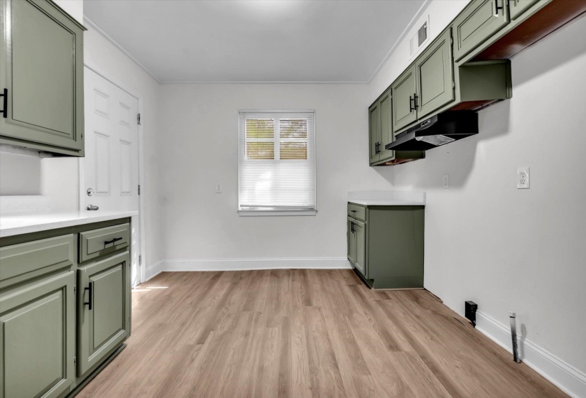 Kitchenette featuring wood-finish flooring, sage green cabinetry with black hardware, white countertops, and a window with a white blind