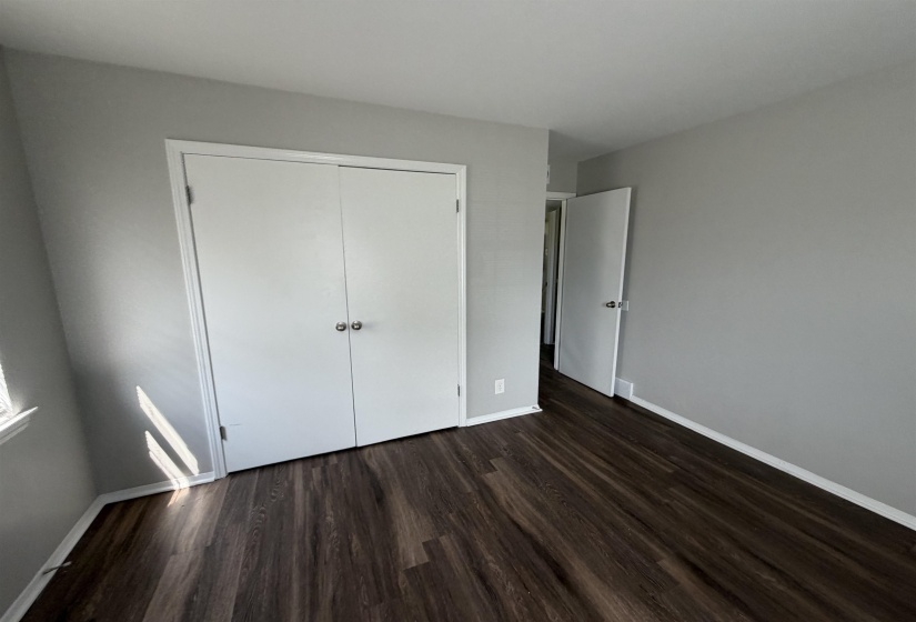 Interior room featuring wood-finish flooring, light grey painted walls, white baseboards, and a white bi-fold closet door