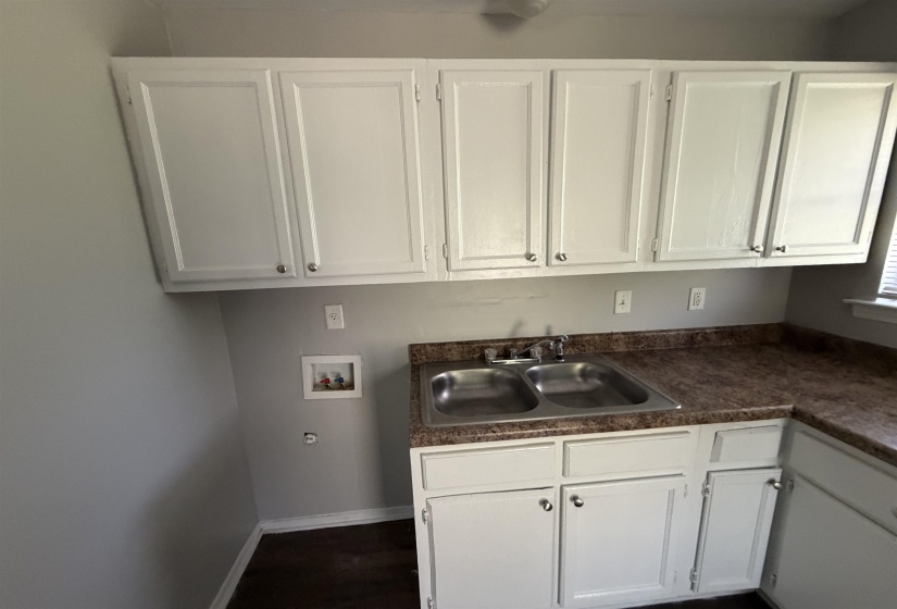 Utility area featuring white shaker-style cabinetry, a double basin stainless steel sink, a patterned laminate countertop, and wood-finish flooring