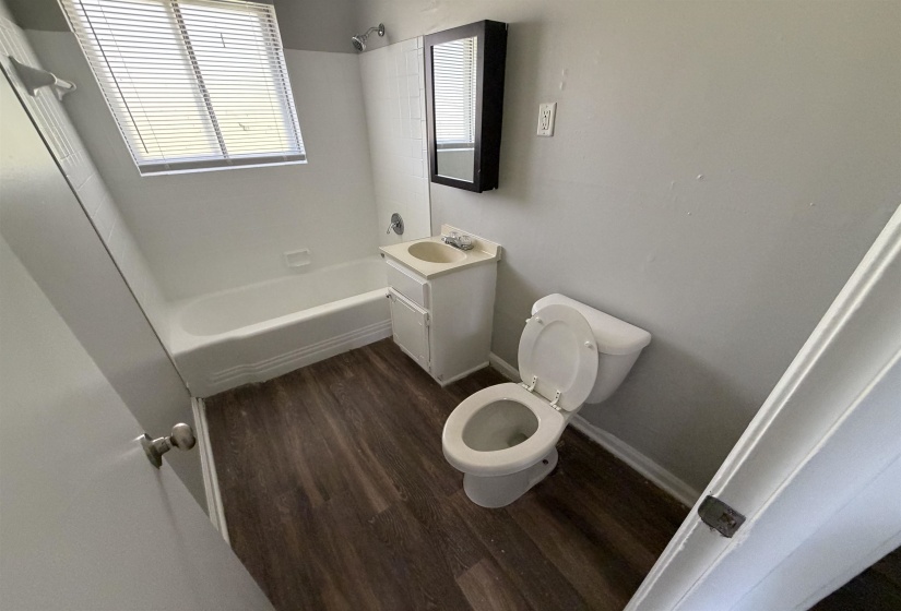Bathroom featuring wood-finish flooring, a white bathtub with tile surround, a single vanity with storage, and a framed wall mirror