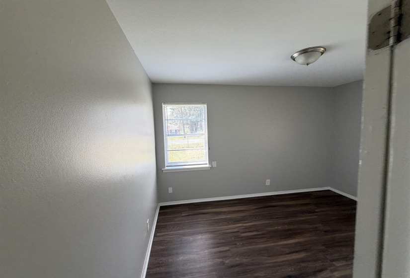 Room featuring wood-finish flooring, neutral gray walls, a window with exterior views, white baseboards, and a semi-flush mount ceiling light