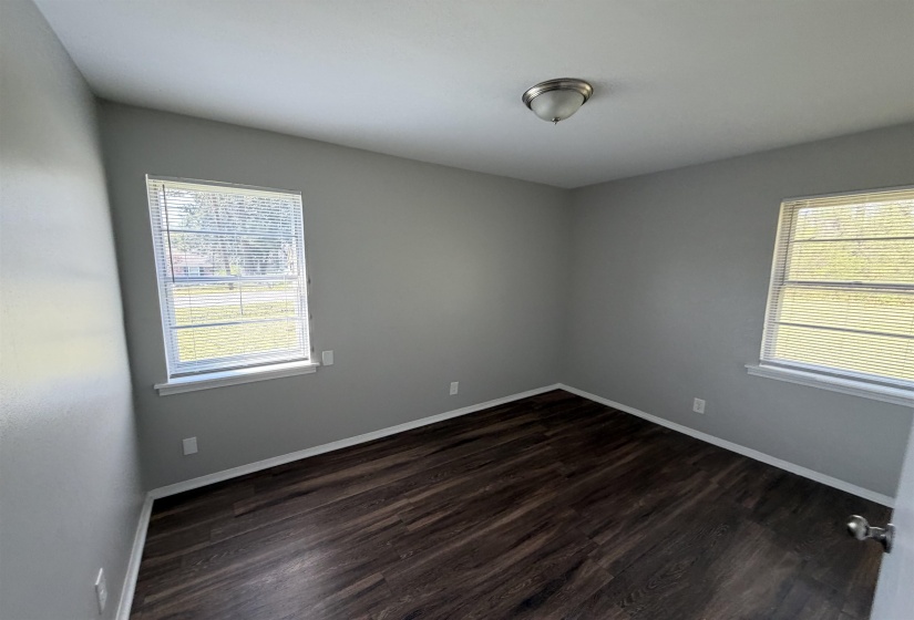 Room featuring wood-finish flooring, light gray walls, white baseboards, and two windows with blinds