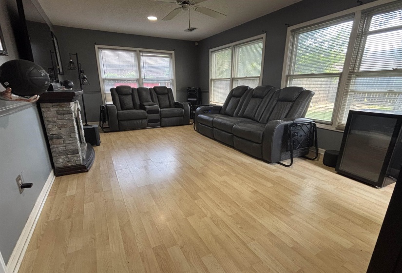 Living area featuring light wood-finish flooring, a ceiling fan, and multiple windows with blinds
