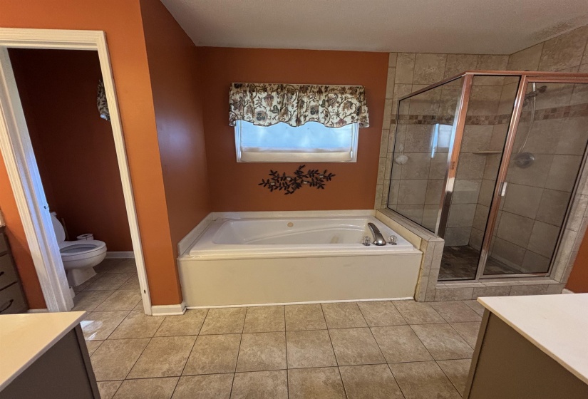 Tiled bathroom featuring a built-in jetted tub, a separate glass-enclosed shower with tiled walls, and a window for natural light