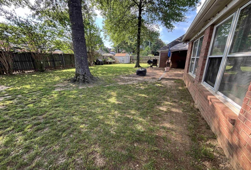 Expansive rear yard featuring mature trees, a privacy fence, and a brick exterior with multiple windows