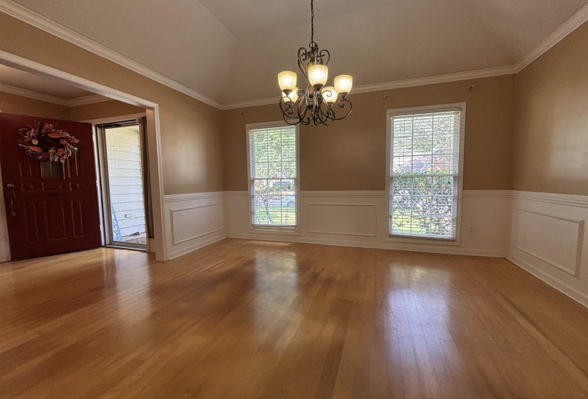 Spacious interior room featuring wood-finish flooring, white wainscoting, and a decorative chandelier
